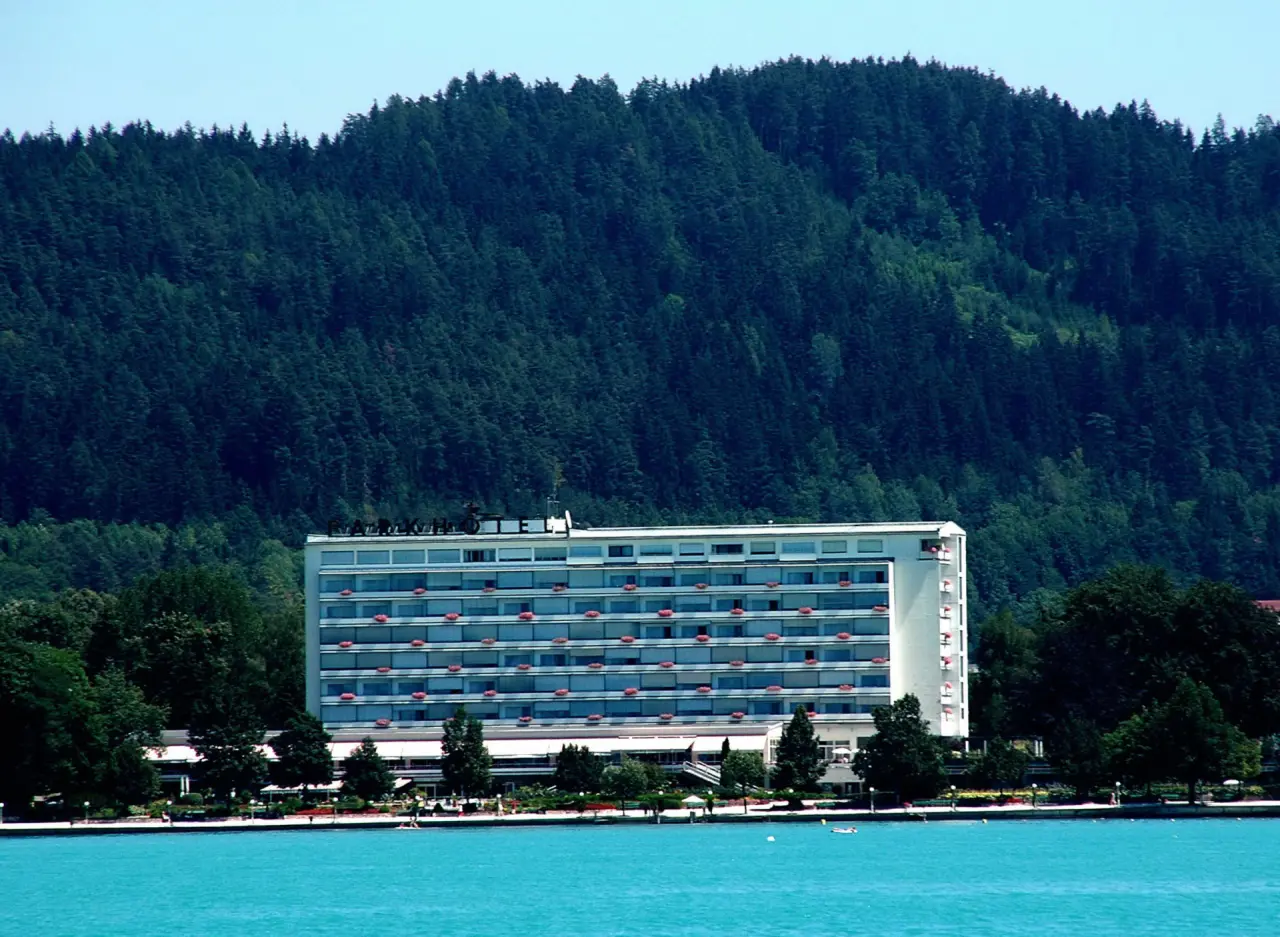 Aussenansicht des Parkhotel Pörtschach am Wörthersee mit bewaldeten Bergen im Hintergrund und blauem See.