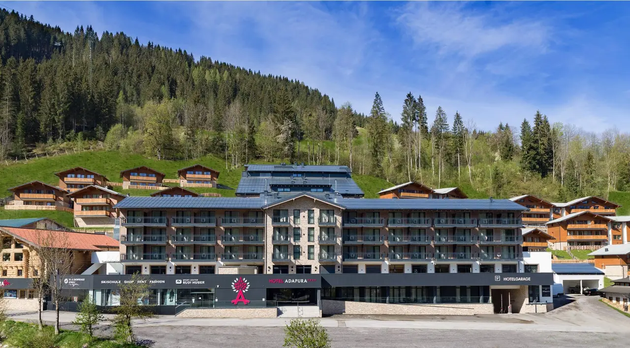 Aussenansicht des modernen Hotel Adapura Wagrain mit umliegenden Chalets vor grünen Bergen und Wald.
