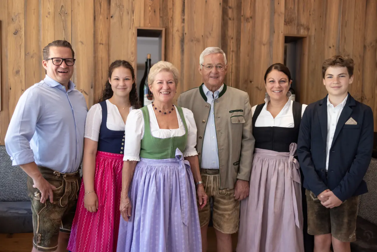 Die freundliche Hoteliersfamilie des Hotel Rauriserhof in traditioneller Tracht vor einer Holzwand.