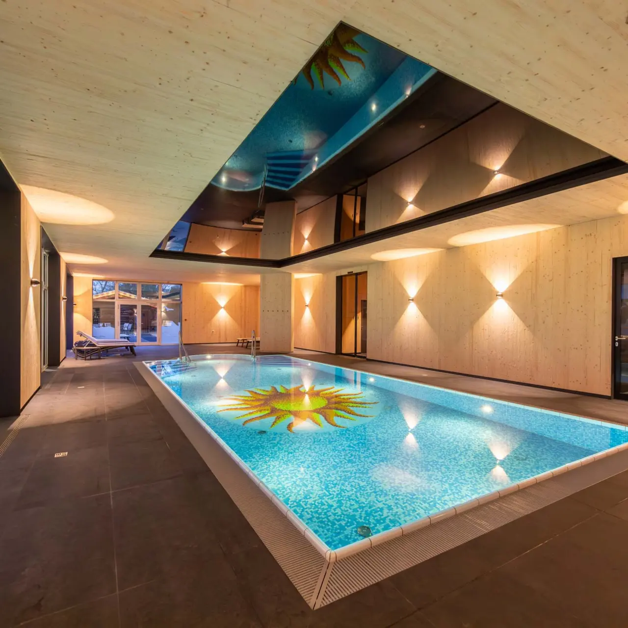 Modernes Hallenbad mit Holzverkleidung, Sonnen-Mosaik und reflektierender Decke im Fair Hotel. Entspannung pur.