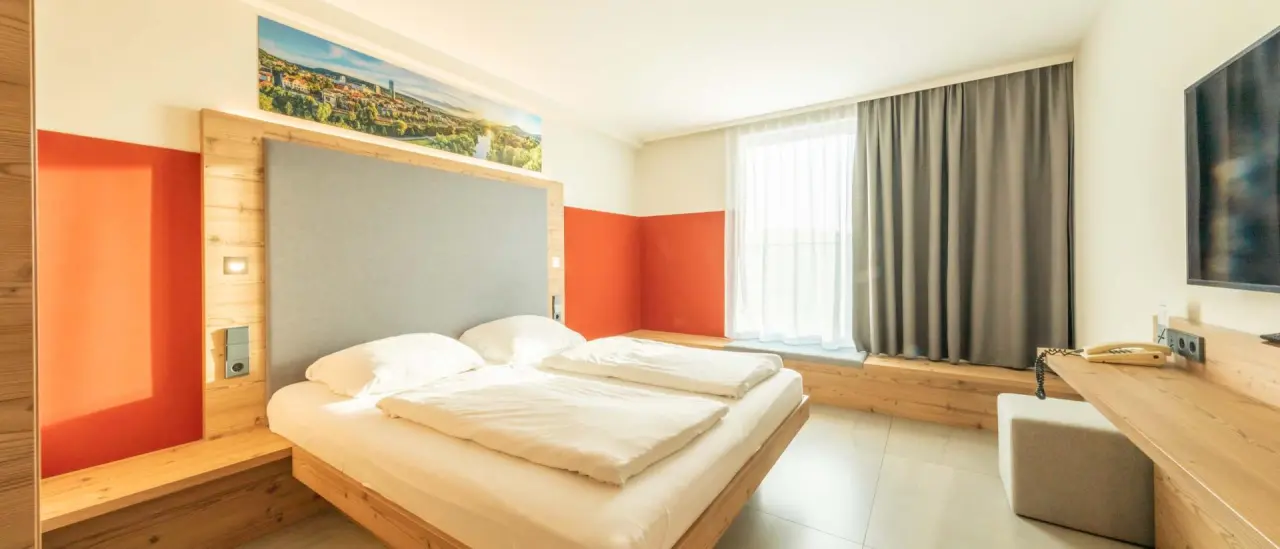 Modernes Doppelzimmer im Fair Hotel mit Holzelementen, bequemen Betten und Stadtpanorama-Wandbild.