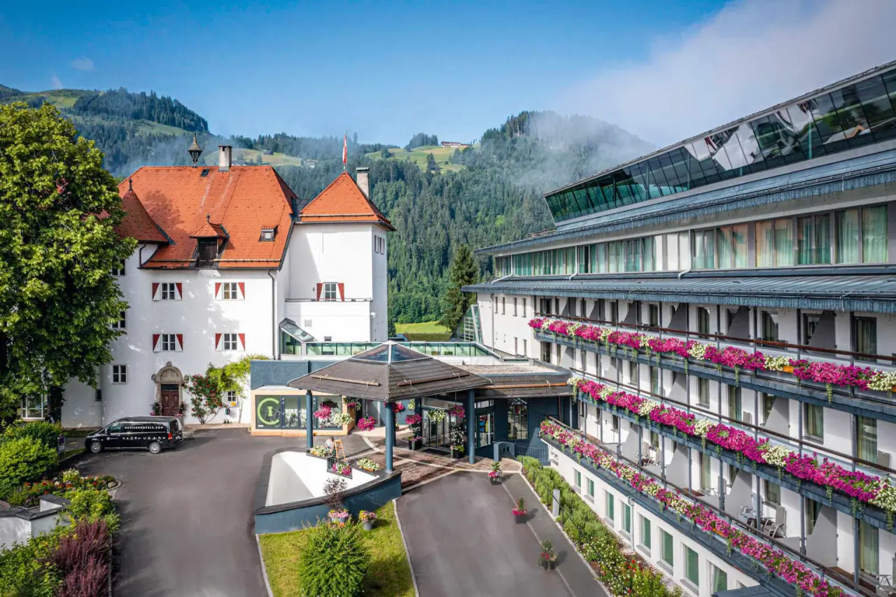 Majestätisches Lebenberg Schlosshotel in Kitzbühel mit historischem und modernem Bau, blühenden Balkonen und Alpenpanorama.
