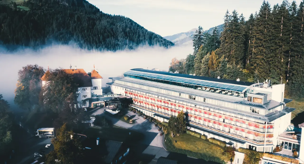 Majestätisches Lebenberg Schlosshotel in Kitzbühel, umgeben von nebelverhangenen Bergen und Wäldern.