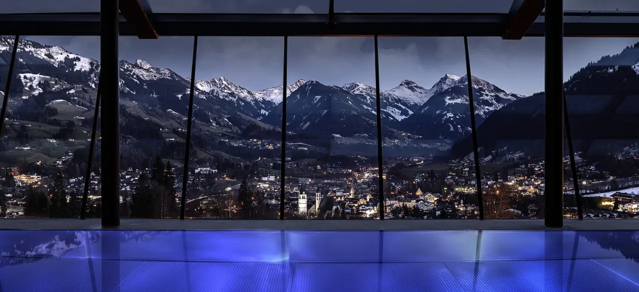 Infinity Pool mit Panoramablick auf Kitzbühel und die verschneiten Alpen im Lebenberg Schlosshotel bei Dämmerung.