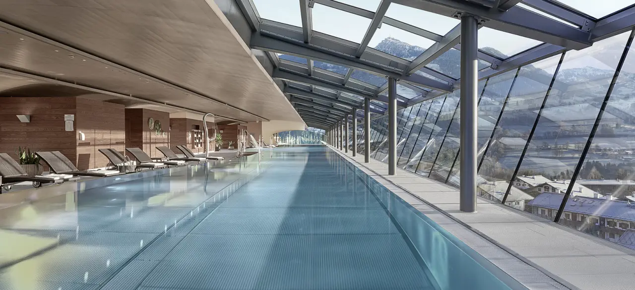 Panoramischer Indoor-Pool mit Bergblick im Lebenberg Schlosshotel. Moderner Wellnessbereich mit Glasdach und Liegen.