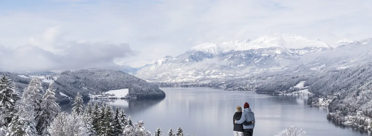 Winterpanorama des Wörthersees mit schneebedeckten Bergen und Paar im Hotel Villa Postillion am See.