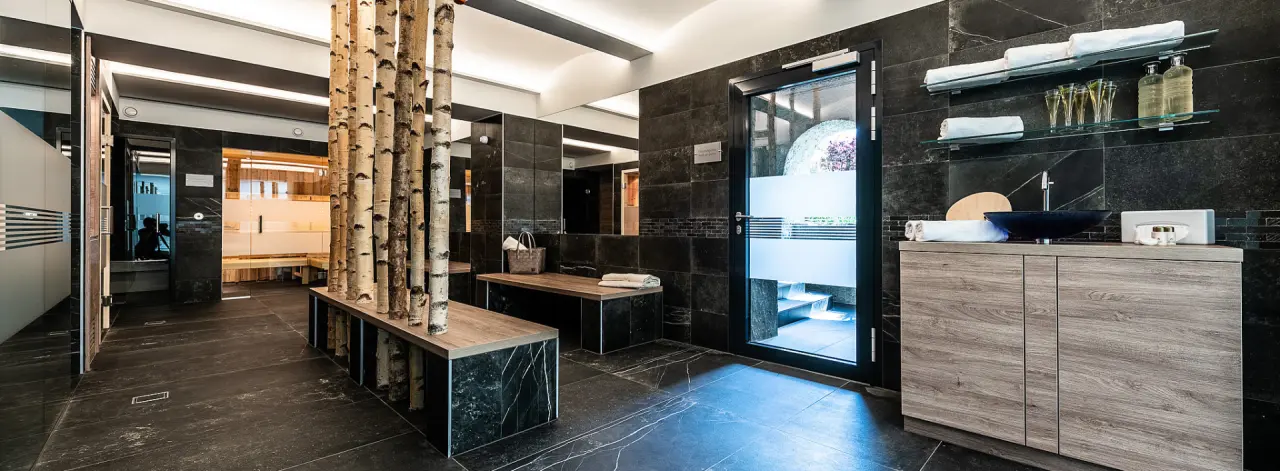 Elegante Spa-Umkleide mit Birkenstämmen, dunklen Natursteinfliesen und Zugang zu Sauna/Dampfbad in der Villa Postillion am See.