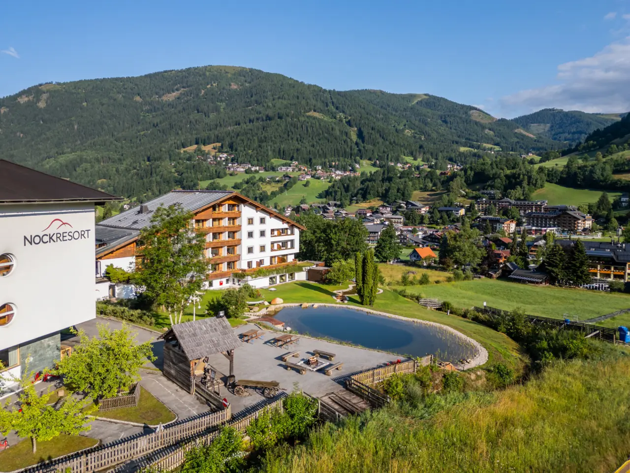 Aussenansicht des Hotel NockResort mit Naturteich, Feuerstelle und Alpenpanorama im Sommer.