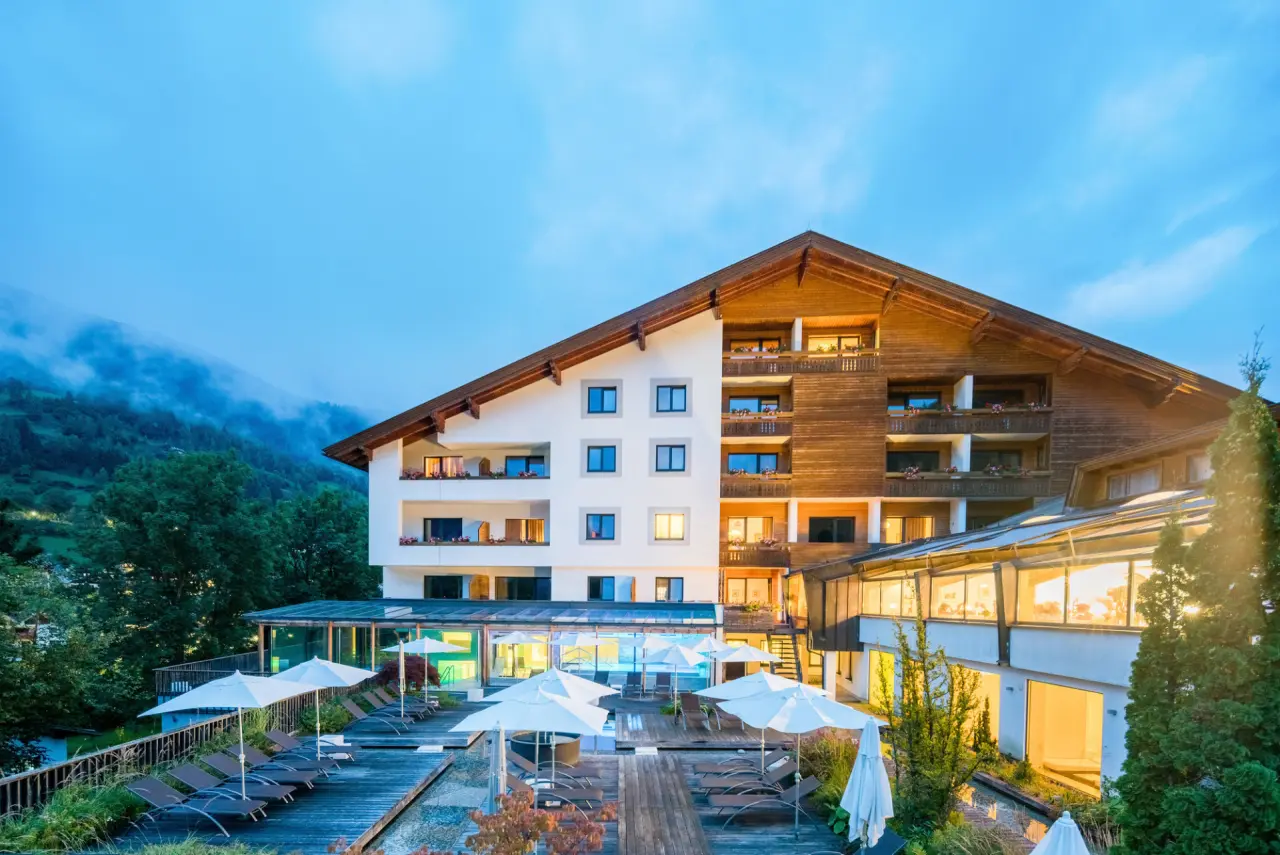 Abendansicht des Hotel NockResort mit beleuchtetem Aussenpool und Liegebereich vor nebelverhangenen Bergen.