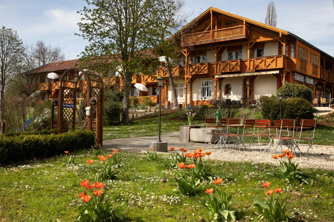 Aussenansicht des Hotel Quellenhof mit traditioneller Holzfassade, Balkonen und einem frühlingshaften Garten mit bunten Tulpen.