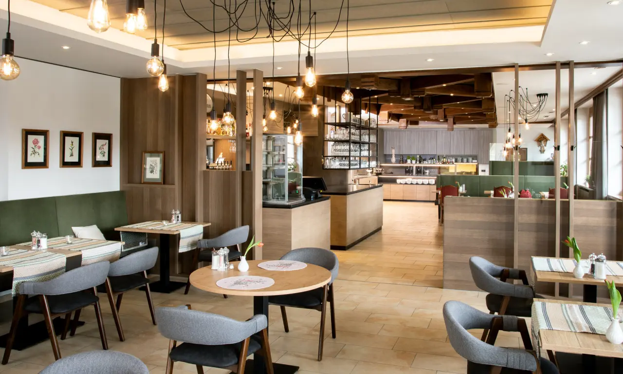 Gemütliches Restaurant mit Holzelementen und modernen Pendelleuchten im Hotel Quellenhof. Ideal für Frühstück und Abendessen.