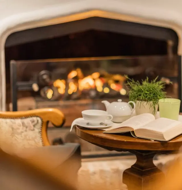 Gemütliche Sitzecke mit Kamin, Teekanne und Buch im Wellnesshotel Schönruh - Adults Only.