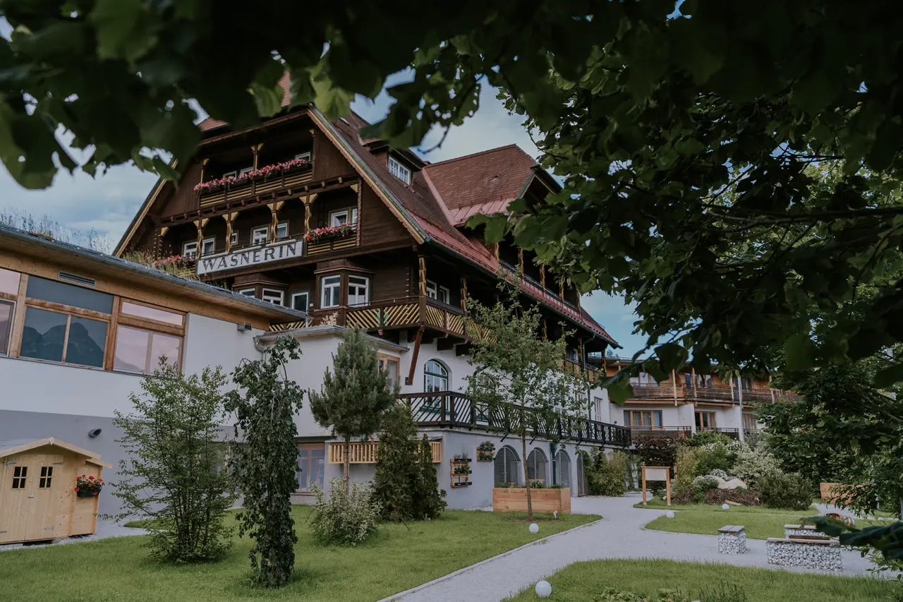 Traditionelles Hotel DIE WASNERIN mit Holzfassade und Gartenweg, umgeben von Bäumen in den Alpen.