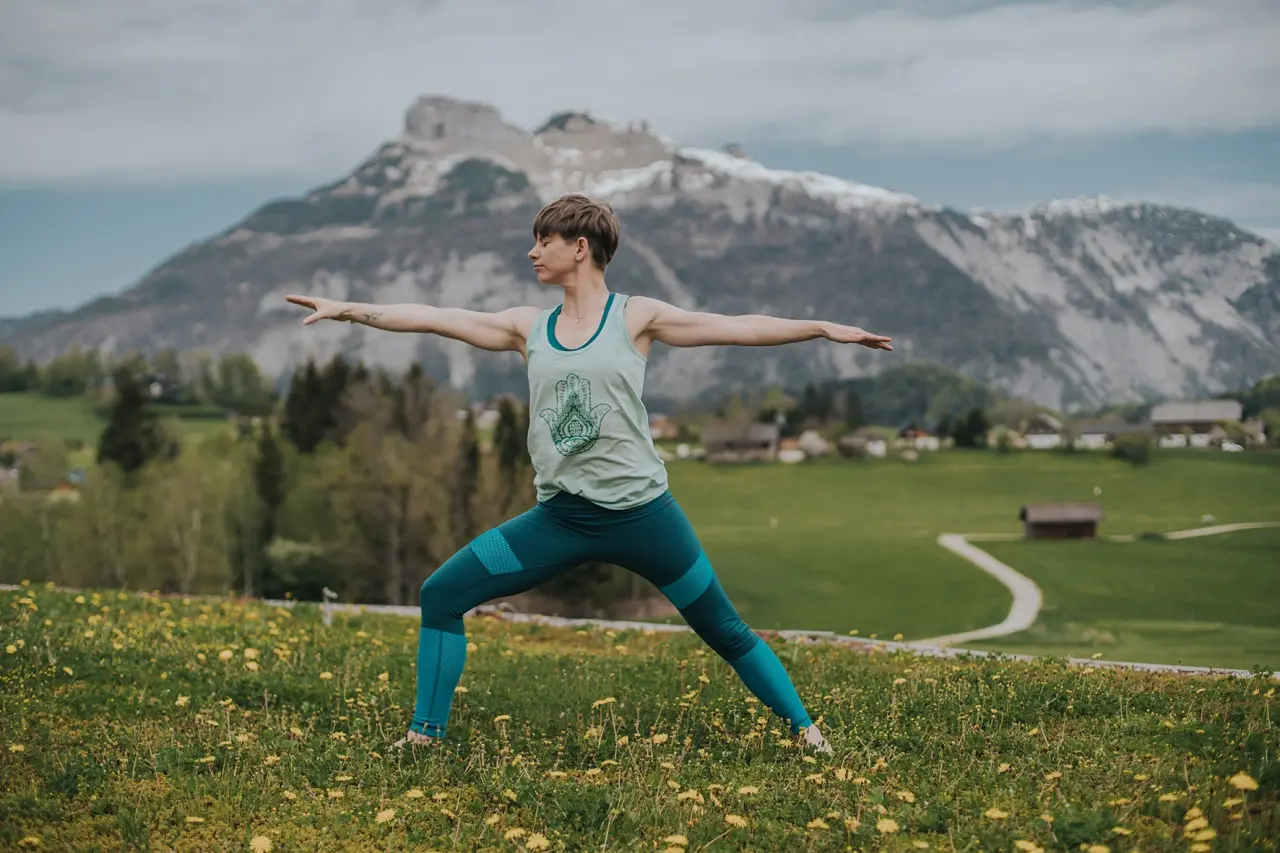 Frau beim Yoga auf einer blühenden Wiese mit majestätischem Bergpanorama im Wellnesshotel DIE WASNERIN.
