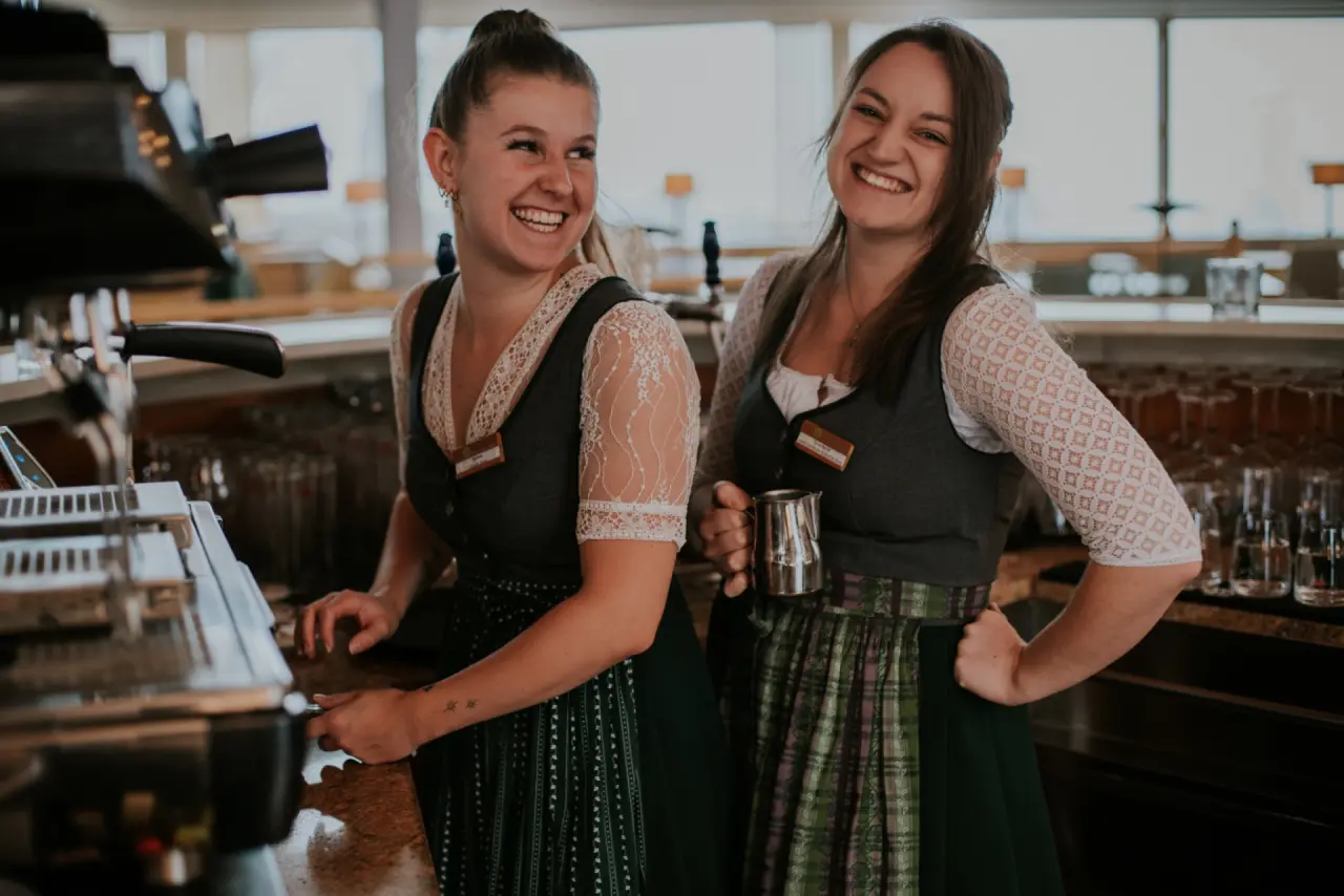 Lachende Mitarbeiterinnen in Tracht hinter der Bar des Hotel DIE WASNERIN, die Gäste herzlich willkommen heißen.