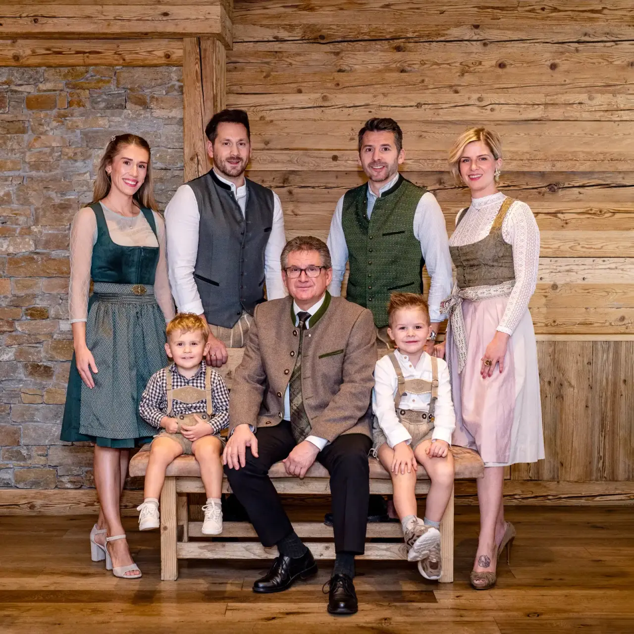 Familienportrait der Gastgeber des Natur- & Wellnesshotel Brunner Hof ****S in traditioneller Tracht vor Holzwand.