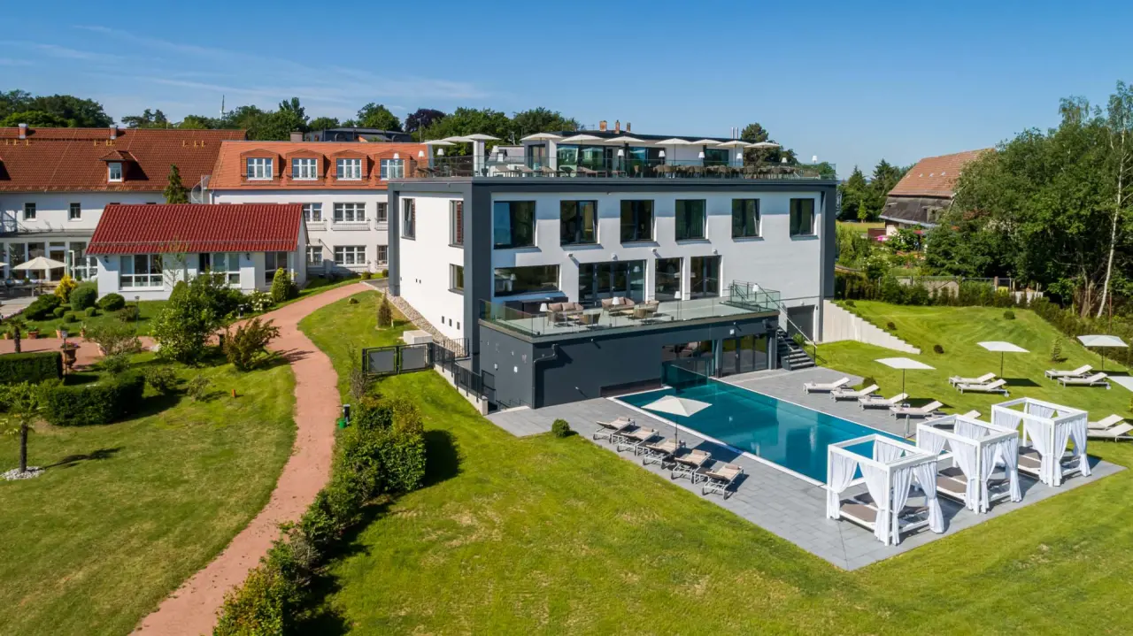 Moderne Aussenansicht des Romantik Hotel Schwanefeld & Spa mit Aussenpool, Sonnenliegen und Cabanas im gruenen Garten.
