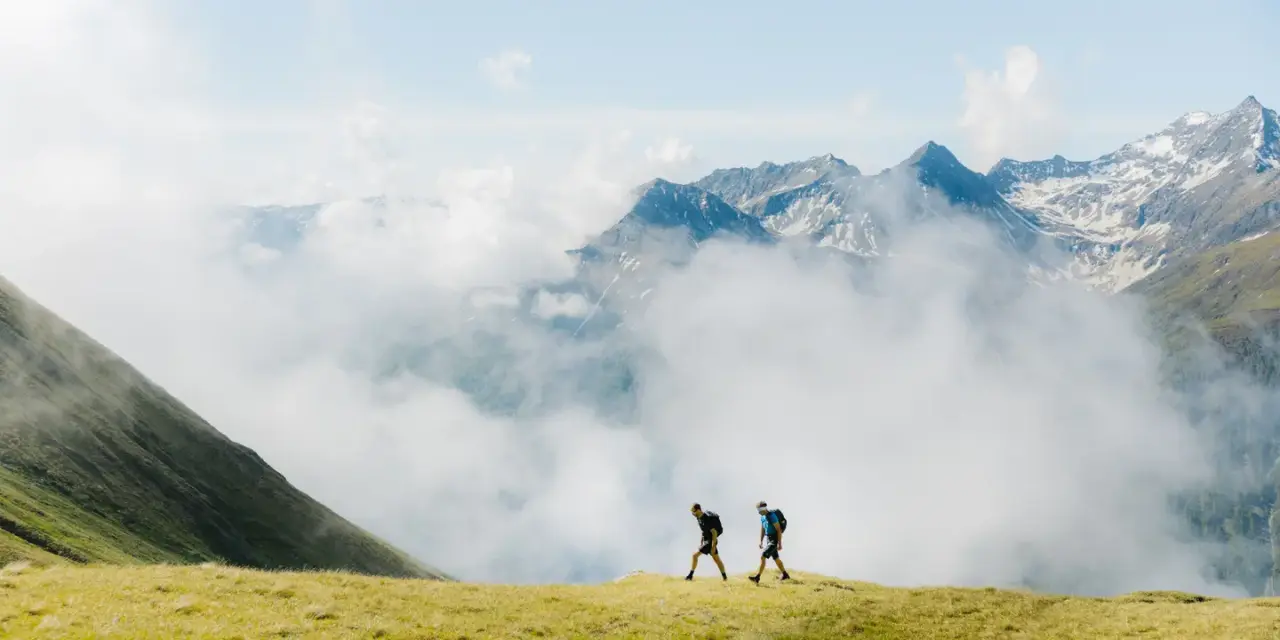 Zwei Wanderer in den majestätischen Bergen mit Wolkenmeer, symbolisch für das Naturhotel Outside Erlebnis.