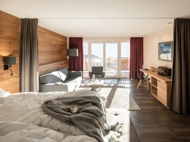 Geräumiges Hotelzimmer im Naturhotel Outside mit Holzwänden, gemütlichem Sofa, Schreibtisch und Balkon mit Bergblick.