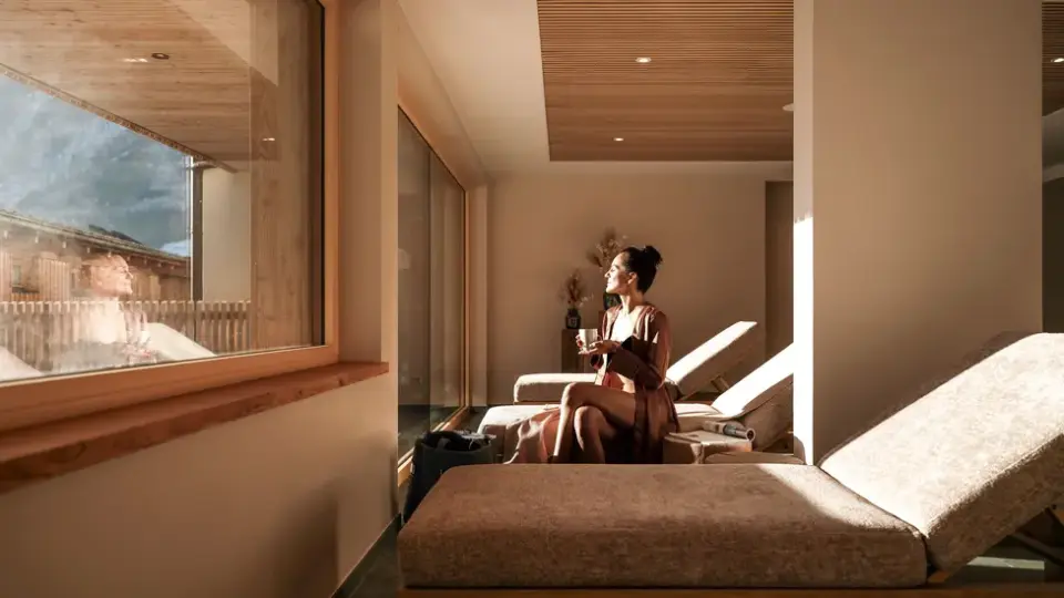 Entspannungsbereich im Naturhotel Outside mit Gast auf Liege, Blick auf die Bergwelt. Gemütliche Spa-Lounge mit Holzelementen.