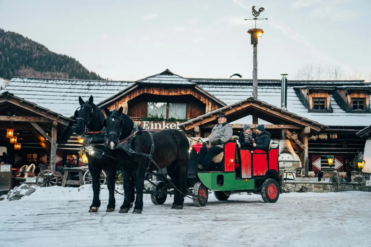 Pferdeschlittenfahrt vor dem traditionellen Hotel GUT Trattlerhof & Chalets im winterlichen Bad Kleinkirchheim.