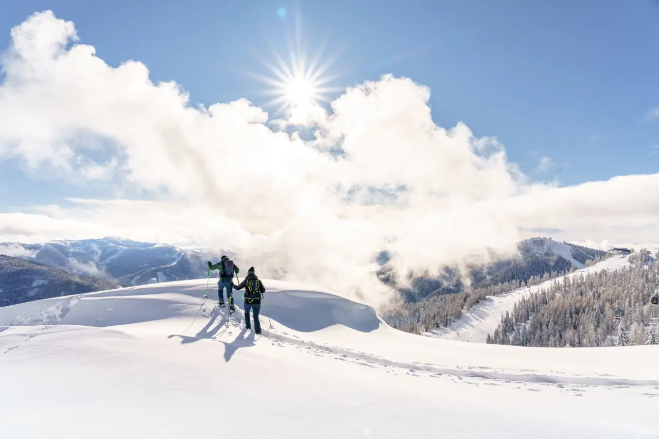 Skitourengeher im tiefen Schnee mit strahlender Sonne und Bergpanorama bei Hotel GUT Trattlerhof & Chalets.