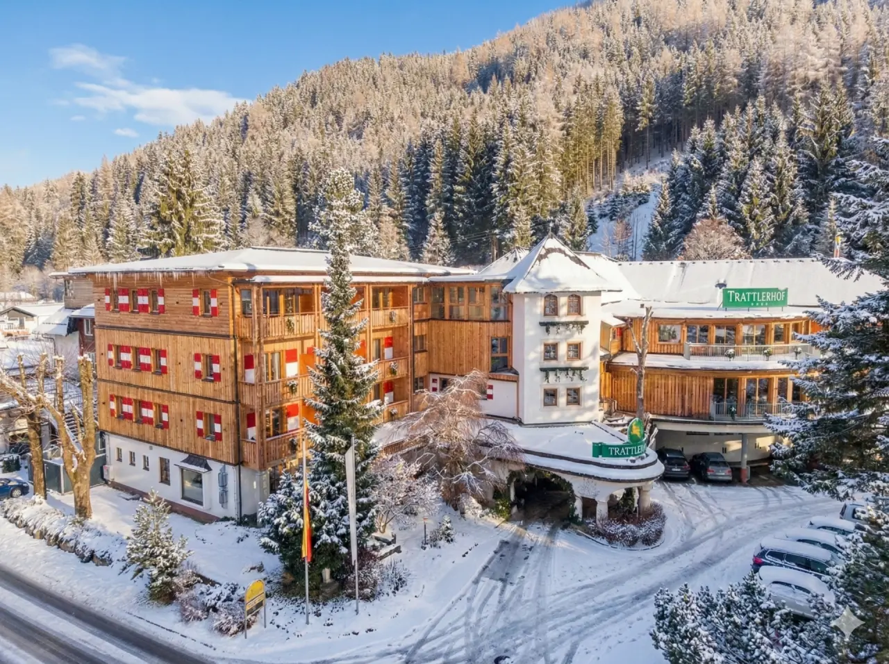 Hotel GUT Trattlerhof & Chalets im Winter: Traditionelles Gebäude mit roten Fensterläden, umgeben von verschneitem Wald.