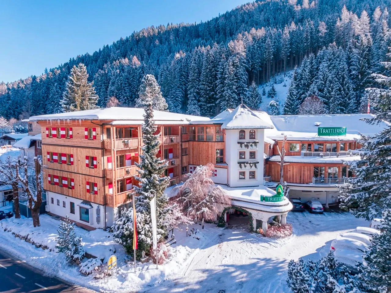 Hotel GUT Trattlerhof & Chalets im Winter, umgeben von verschneiten Bäumen und Bergen unter blauem Himmel.