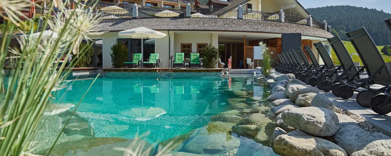 Aussenpool mit Liegen und Felsen im Wellnessbereich des Heselbacher Hofs, umgeben von grüner Natur.