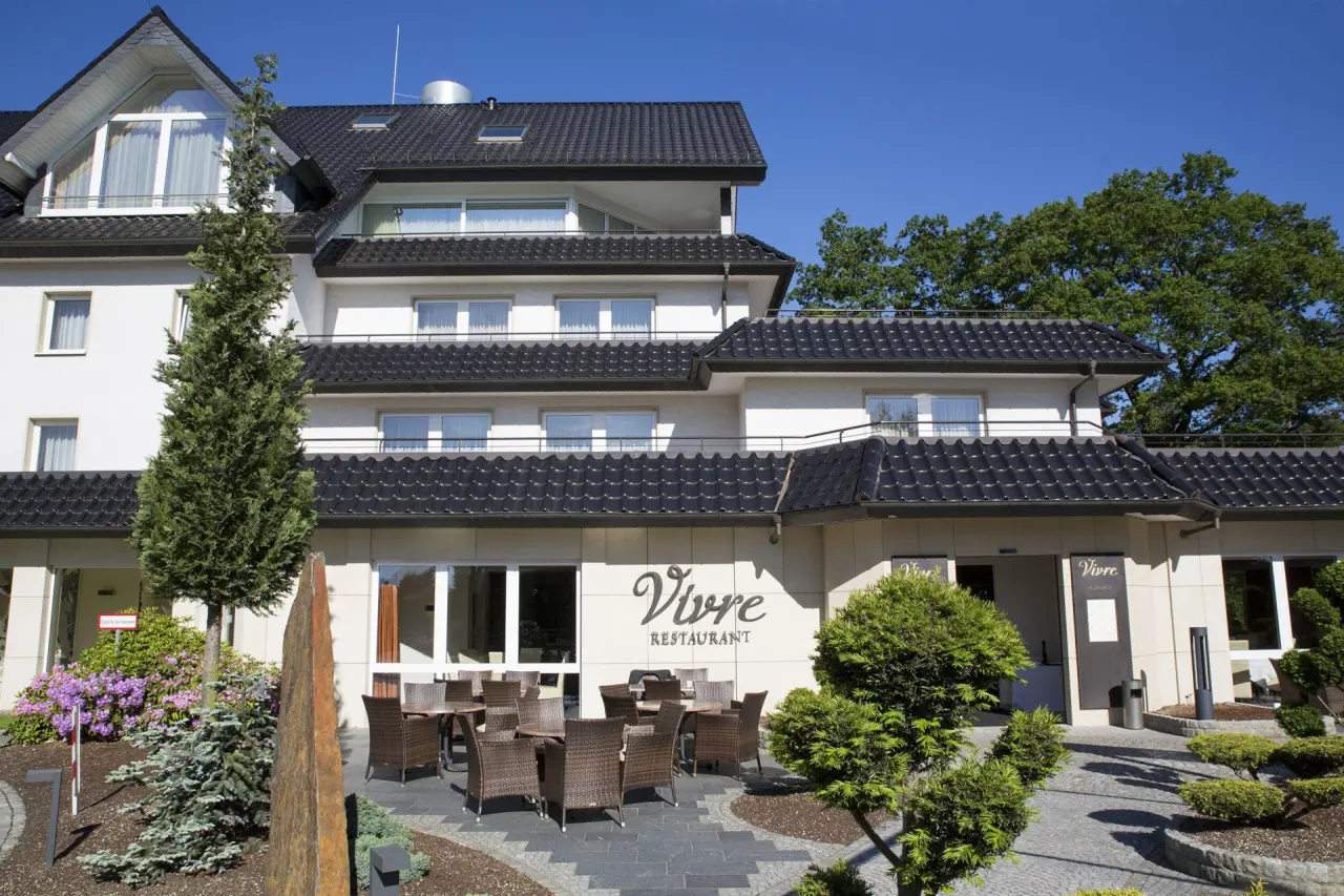 Aussenansicht des l’Arrivée HOTEL & SPA mit Restaurantterrasse und blauer Himmel an einem sonnigen Tag.