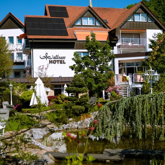 Aussenansicht des Ringhotel Teutoburger Wald mit gepflegtem Garten, Teich und 'Wellness HOTEL' Schriftzug unter blauem Himmel.