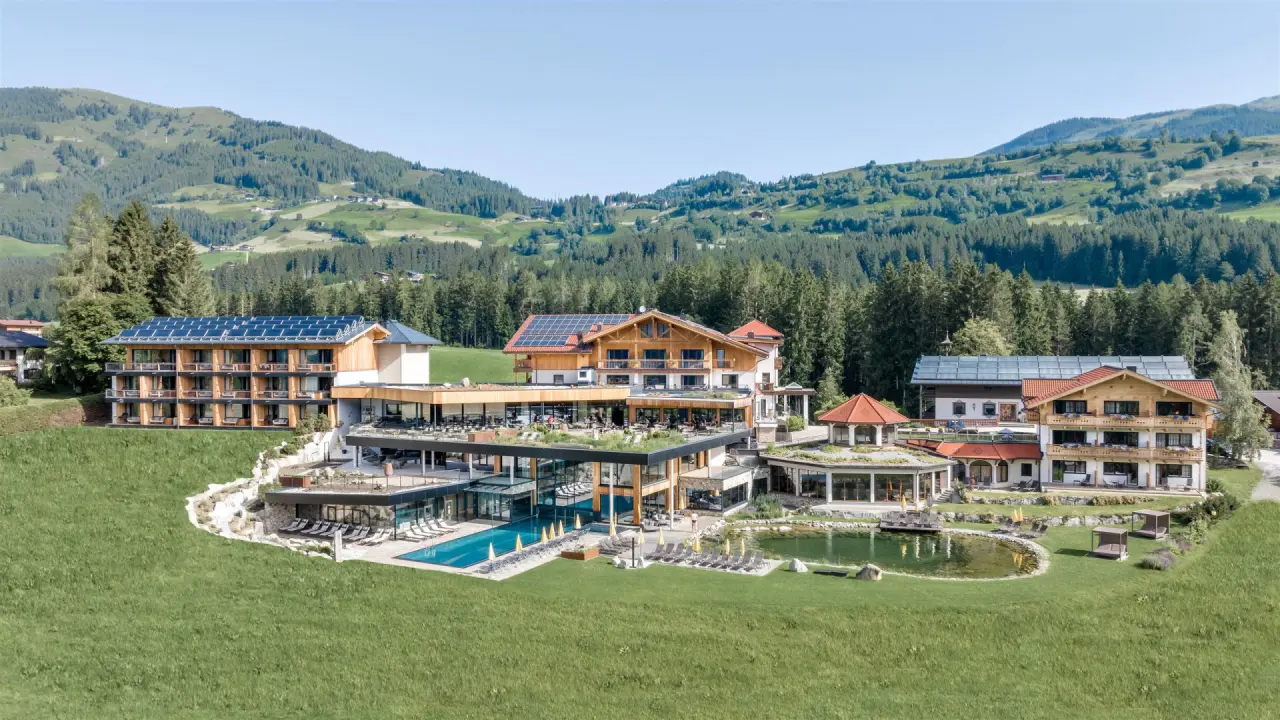 Luftaufnahme des Gut Sonnberghof Naturhotel mit Aussenpool, Naturteich und Bergpanorama im Pinzgau.