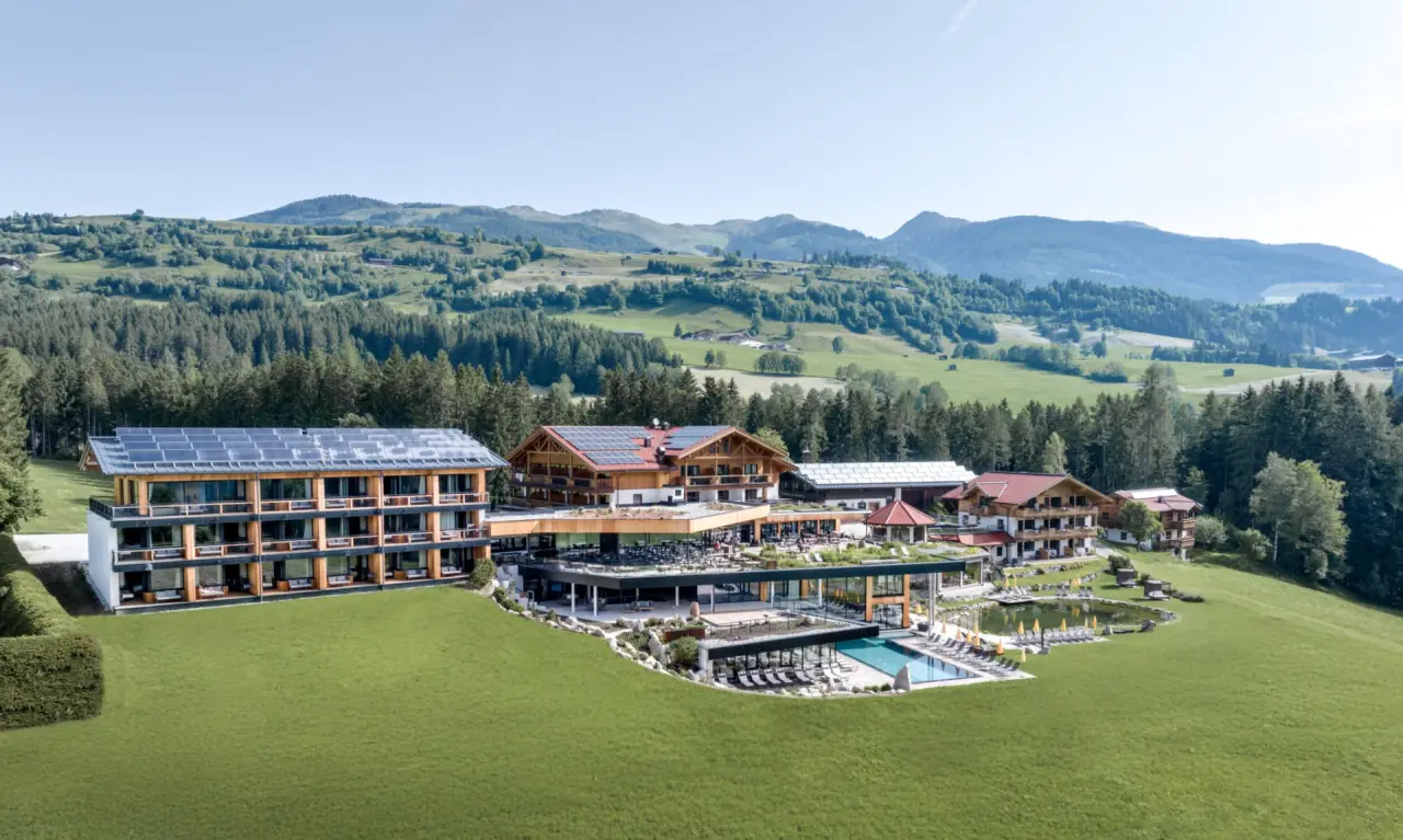 Luftaufnahme des Gut Sonnberghof Naturhotel mit Aussenpool, Naturbadeteich und Bergpanorama in den Kitzbüheler Alpen.