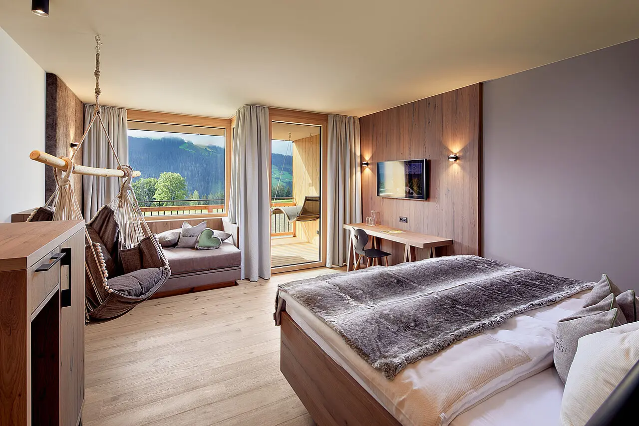Geräumiges Hotelzimmer mit Holzelementen, Hängesessel, Balkon und Bergblick im Gut Sonnberghof Naturhotel.