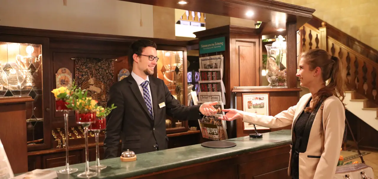 Rezeption des The Lakeside Burghotel zu Strausberg mit lächelndem Personal und Gast beim Check-in.