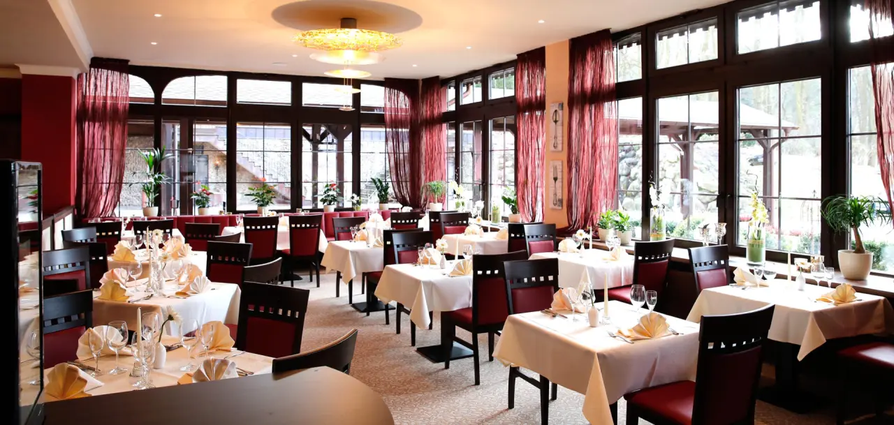 Elegantes Restaurant mit festlich gedeckten Tischen und Blick ins Grüne im The Lakeside Burghotel zu Strausberg.