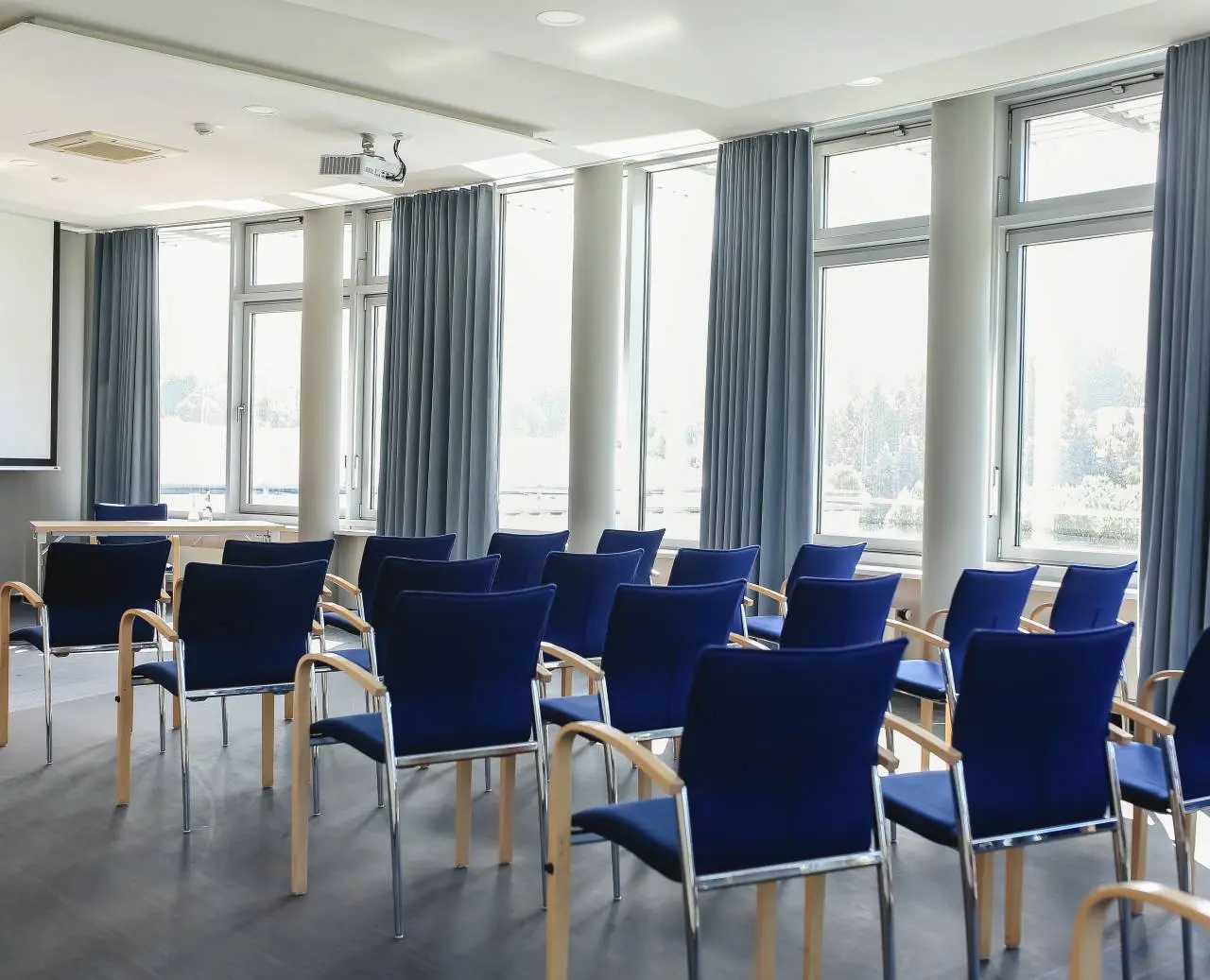 Heller Konferenzraum mit blauen Stühlen, Projektor und großen Fenstern im Hotel am Vitalpark.