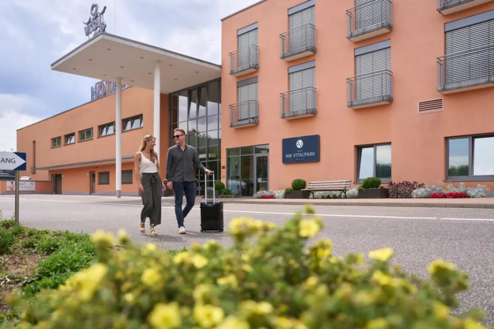 Ankommendes Paar mit Koffer am modernen Eingangsbereich des Hotel am Vitalpark. Gepflegte Aussenansicht des Wellnesshotels.