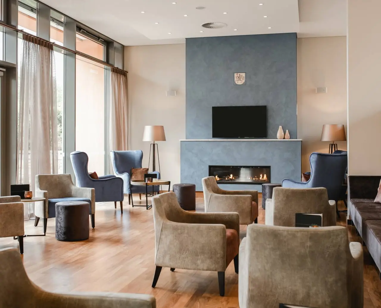 Einladende Hotellobby mit Kamin, bequemen Sesseln und großen Fenstern im Hotel am Vitalpark.