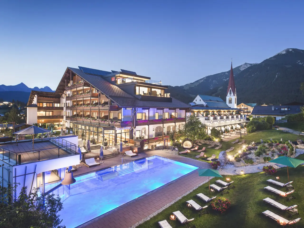 Abendansicht des Hotel Kosterbräu mit beleuchtetem Aussenpool, Garten und Bergpanorama.