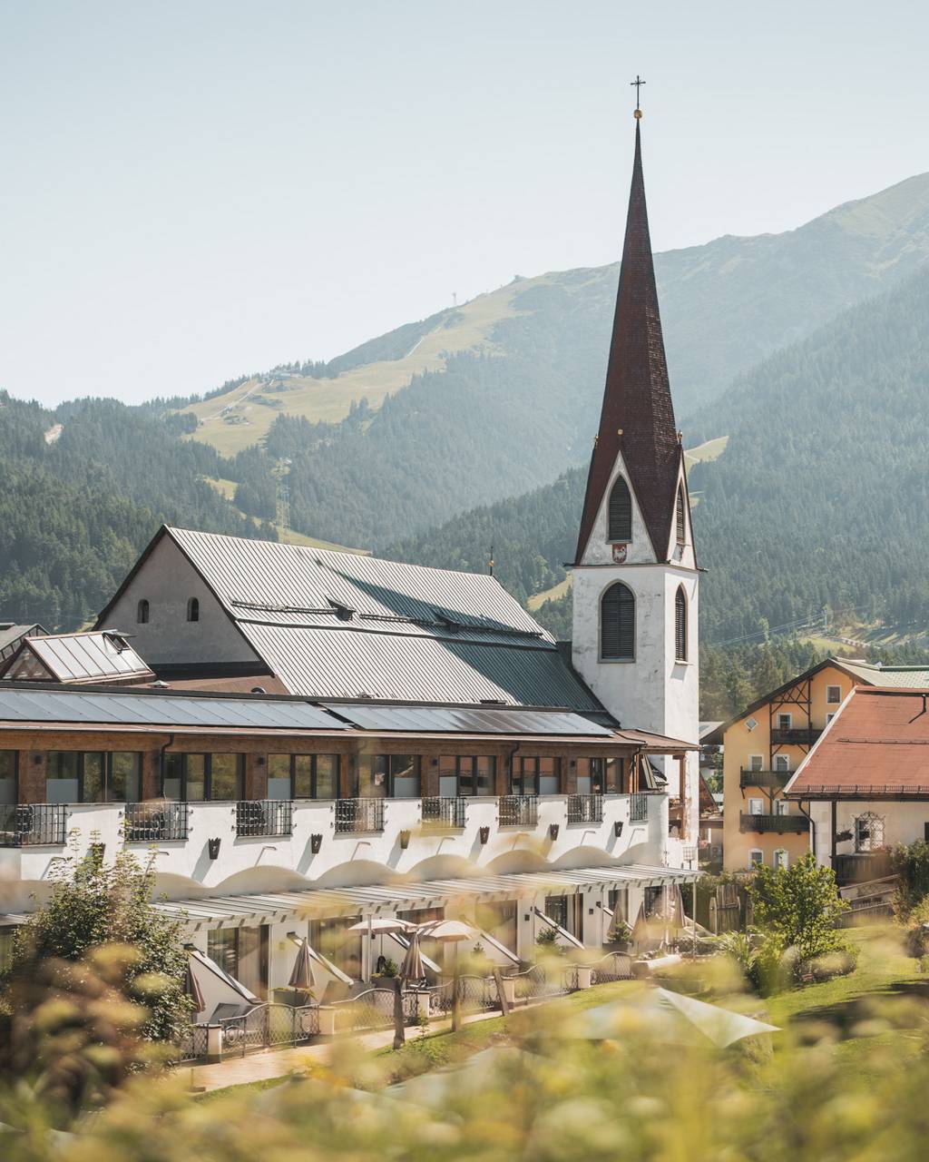 Hotel Kosterbräu in Seefeld – Seitenansicht des Hotels und der Kirche mit Bergen | Wellnesshotel Tirol