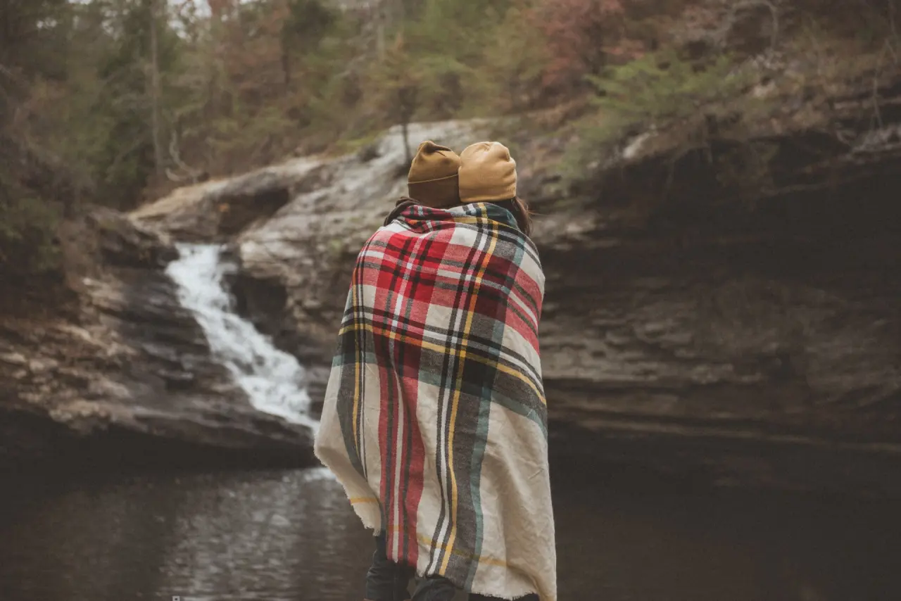 Zwei Personen eingehüllt in Decke blicken auf einen Wasserfall in der Natur, ideal für Entspannung im Bergrose Hideaway.