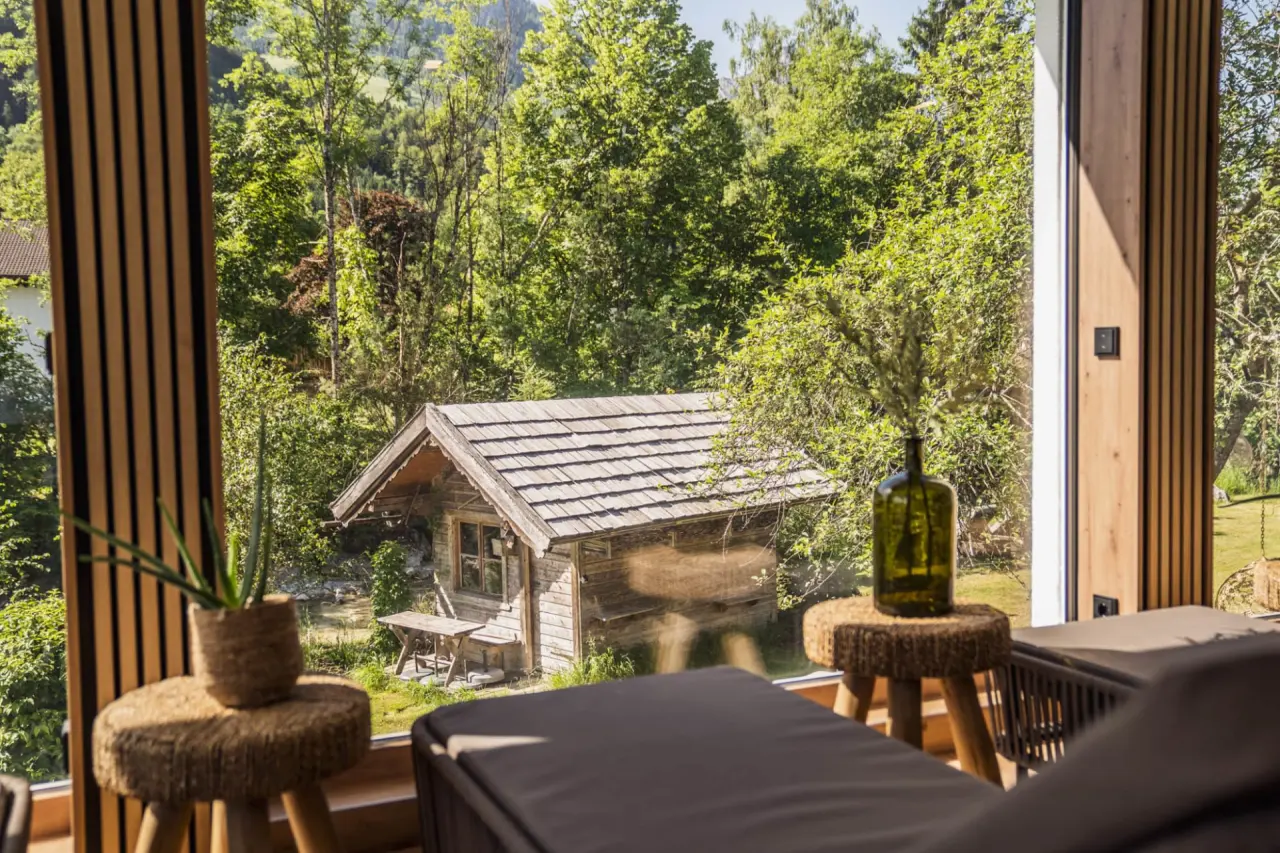 Entspannungsbereich mit bequemen Liegen und Blick auf eine idyllische Holzhütte und grüne Natur im Bergrose Hideaway.