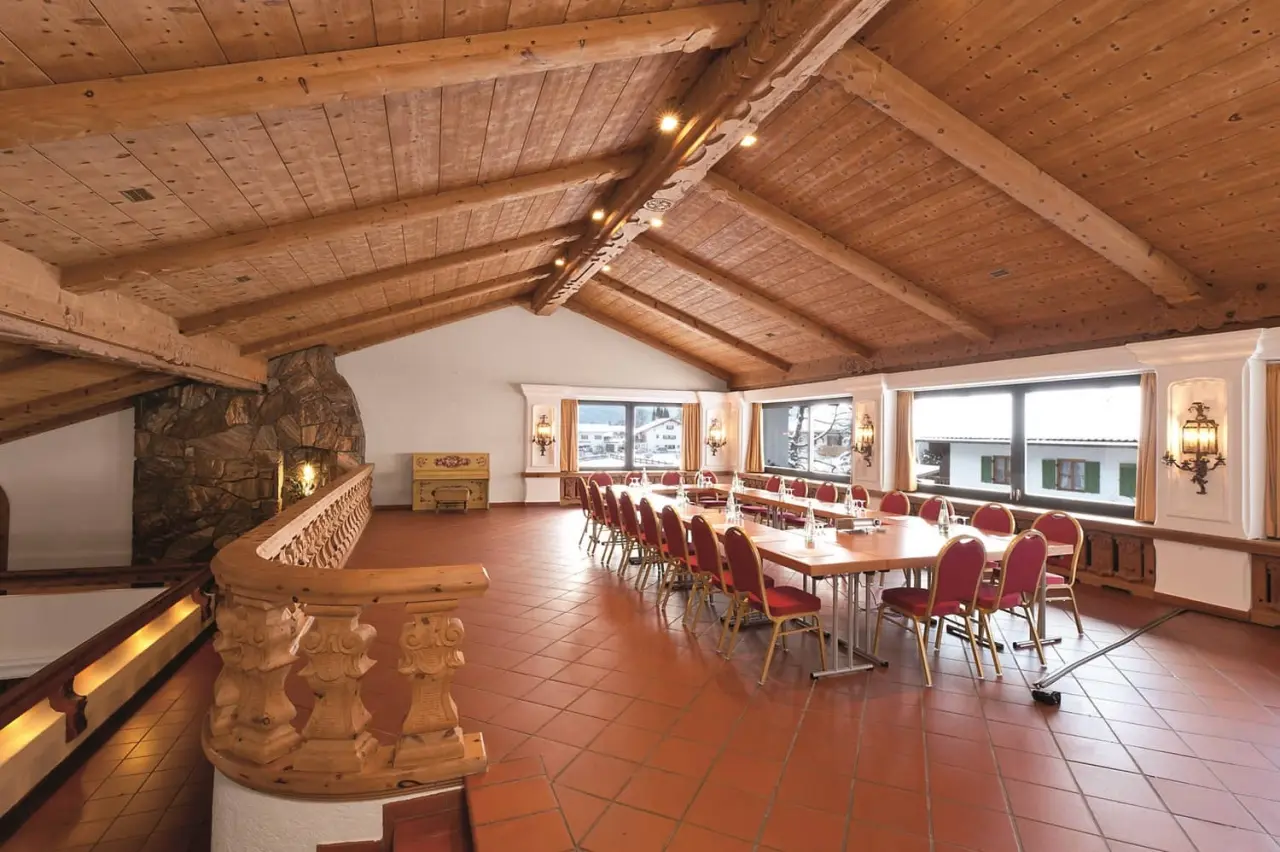 Konferenzraum im Parkhotel Wallgau mit Holzbalkendecke, Steinkamin und Blick auf die verschneite Landschaft.