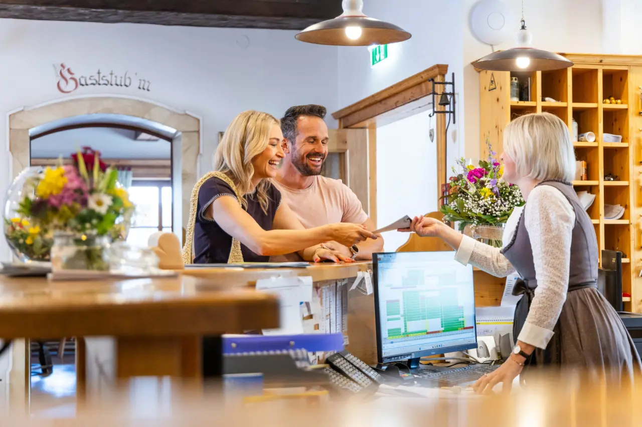 Freundlicher Check-in an der Rezeption des Hotel Bischofsmütze mit lächelnden Gästen und Personal im einladenden Empfangsbereich.