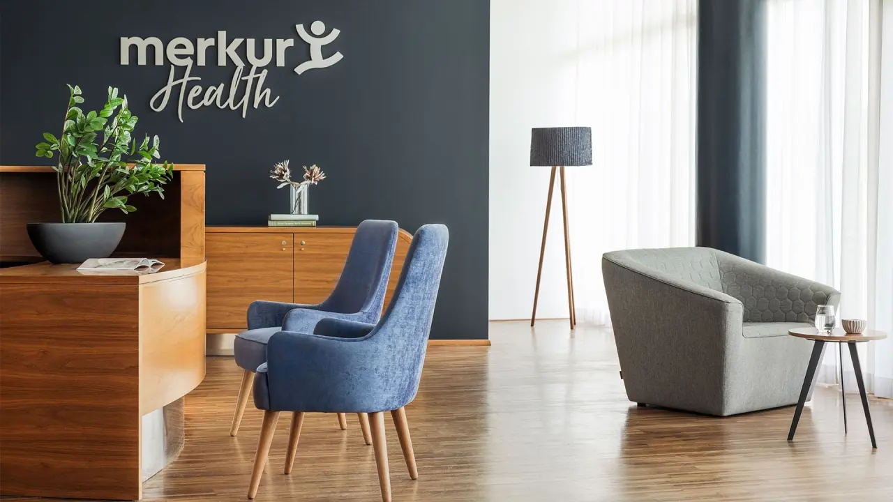 Moderner Wartebereich mit blauen Sesseln und Merkur Health Logo im Falkensteiner Balance Resort Stegersbach.
