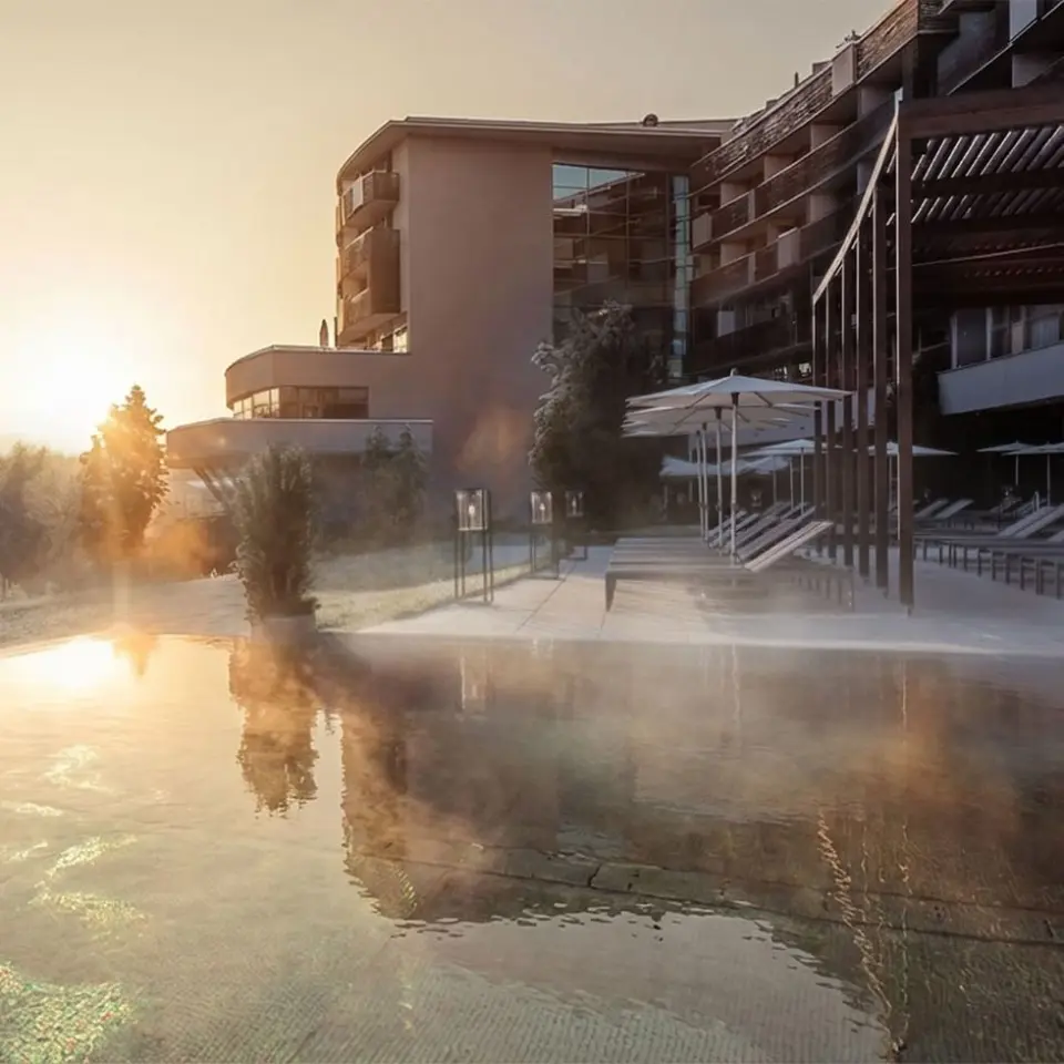 Beheizter Aussenpool mit Dampf und Hotelansicht bei Sonnenaufgang im Falkensteiner Balance Resort Stegersbach.