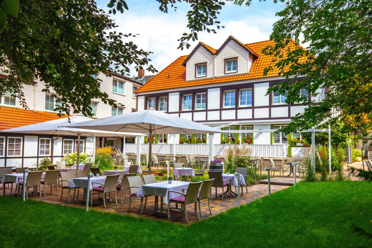 Aussenansicht des traditionellen Hotel Braunschweiger Hof mit Fachwerkfassade und einladender Gartenterrasse unter Sonnenschirmen.