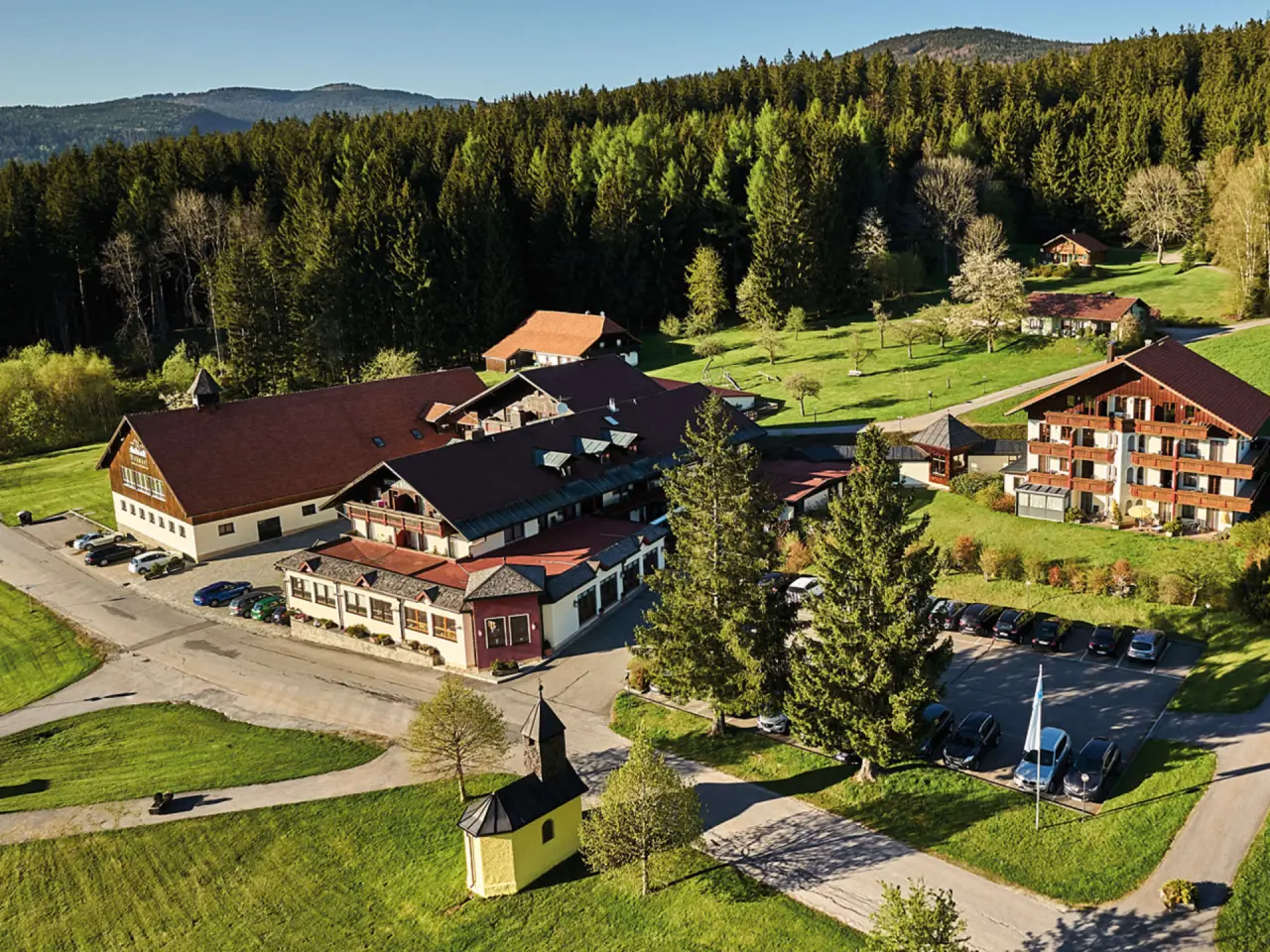 Luftaufnahme des Wellness- und Vitalhotels Böhmhof inmitten grüner Natur mit Wald und Bergen im Bayerischen Wald.