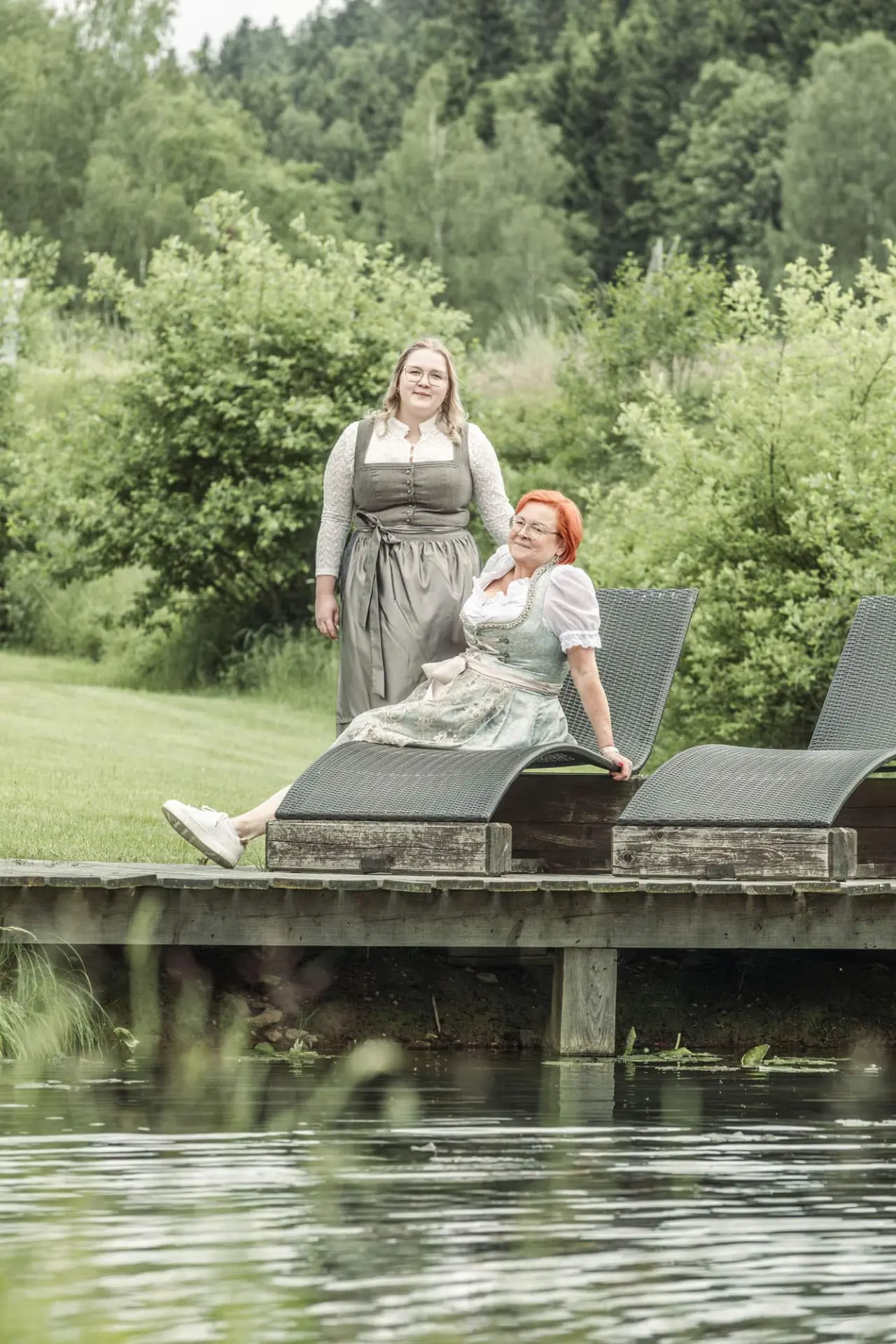 Zwei Frauen in Dirndl entspannen auf Liegen am Teich im Garten des Böhmhof - Wellness- und Vitalhotel.